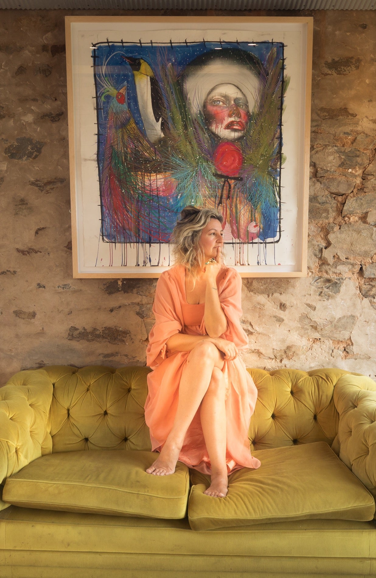 Mariana Mezic sitting on a green couch beneath her artwork